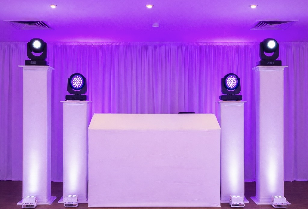 Professional wedding Dj setup with white DJ booth, lighting pillars, pleated white backdrop and uplighting